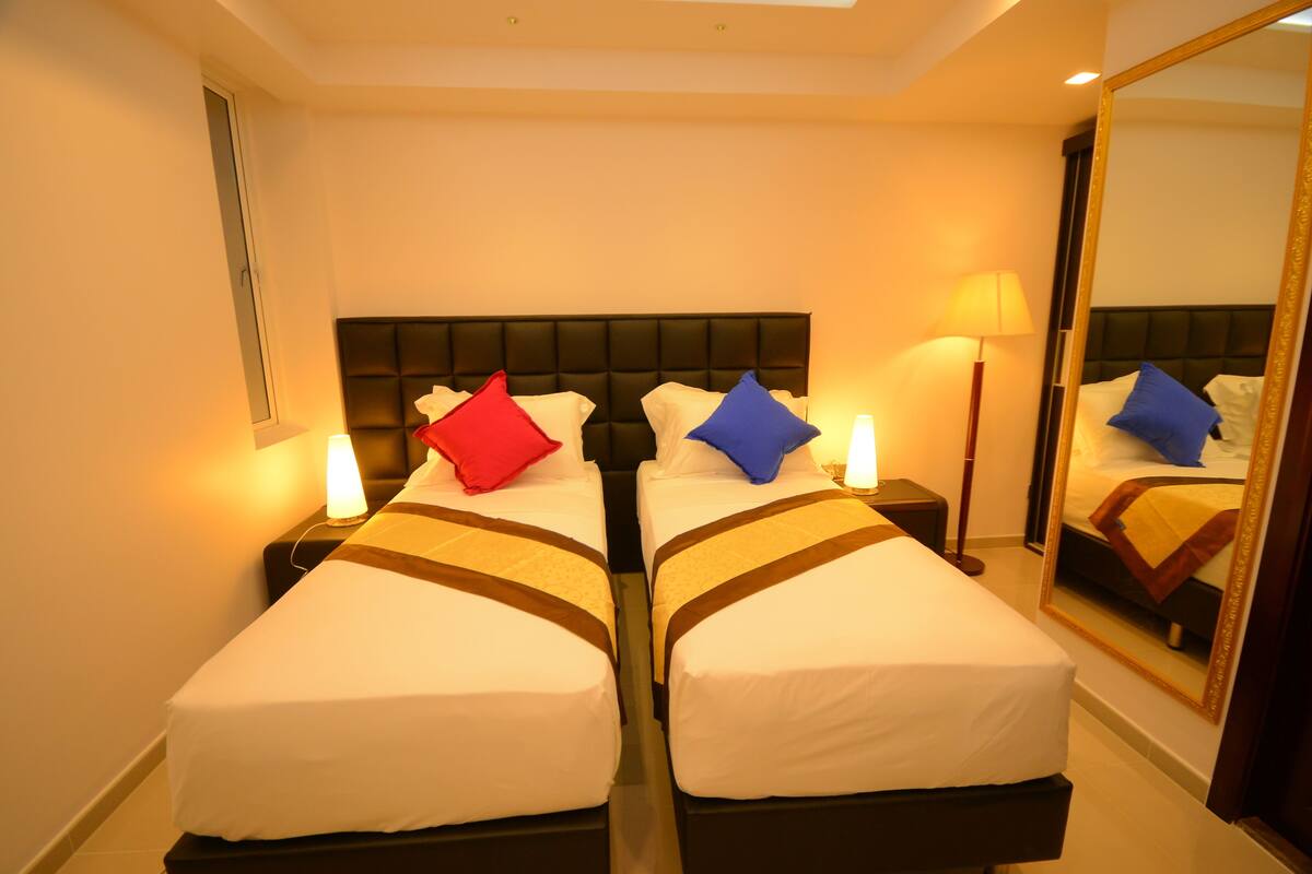 A hotel room with two beds, each with a headboard, bedside lamps, and a mirror on one wall.