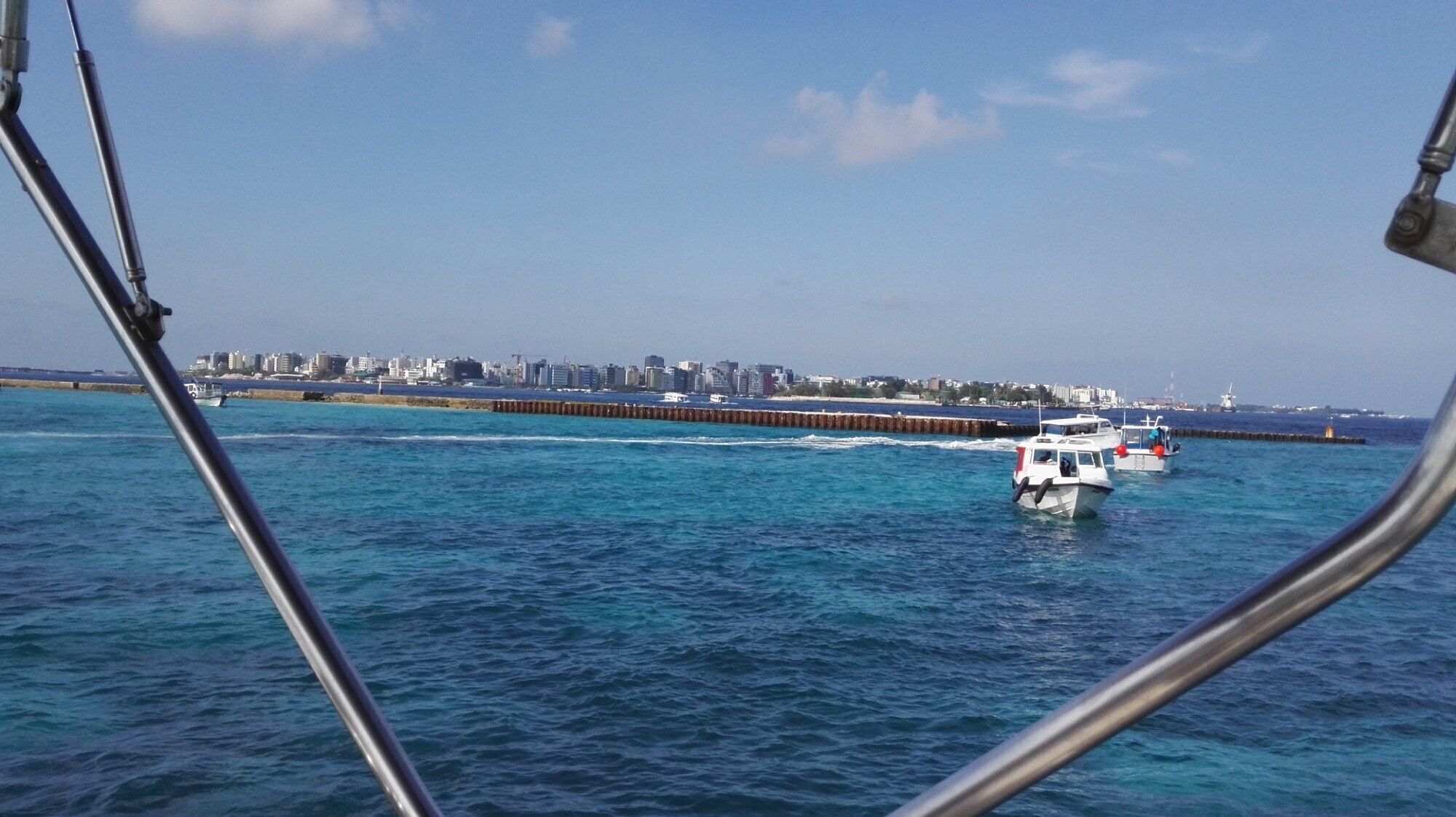 A coastal cityscape with a pier extending into the water, boats, and a clear sky.