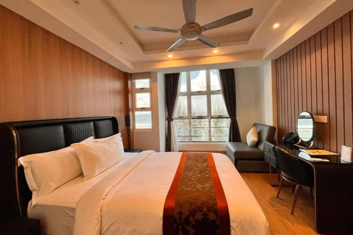 A hotel room with a large bed, a desk, a chair, and a ceiling fan.