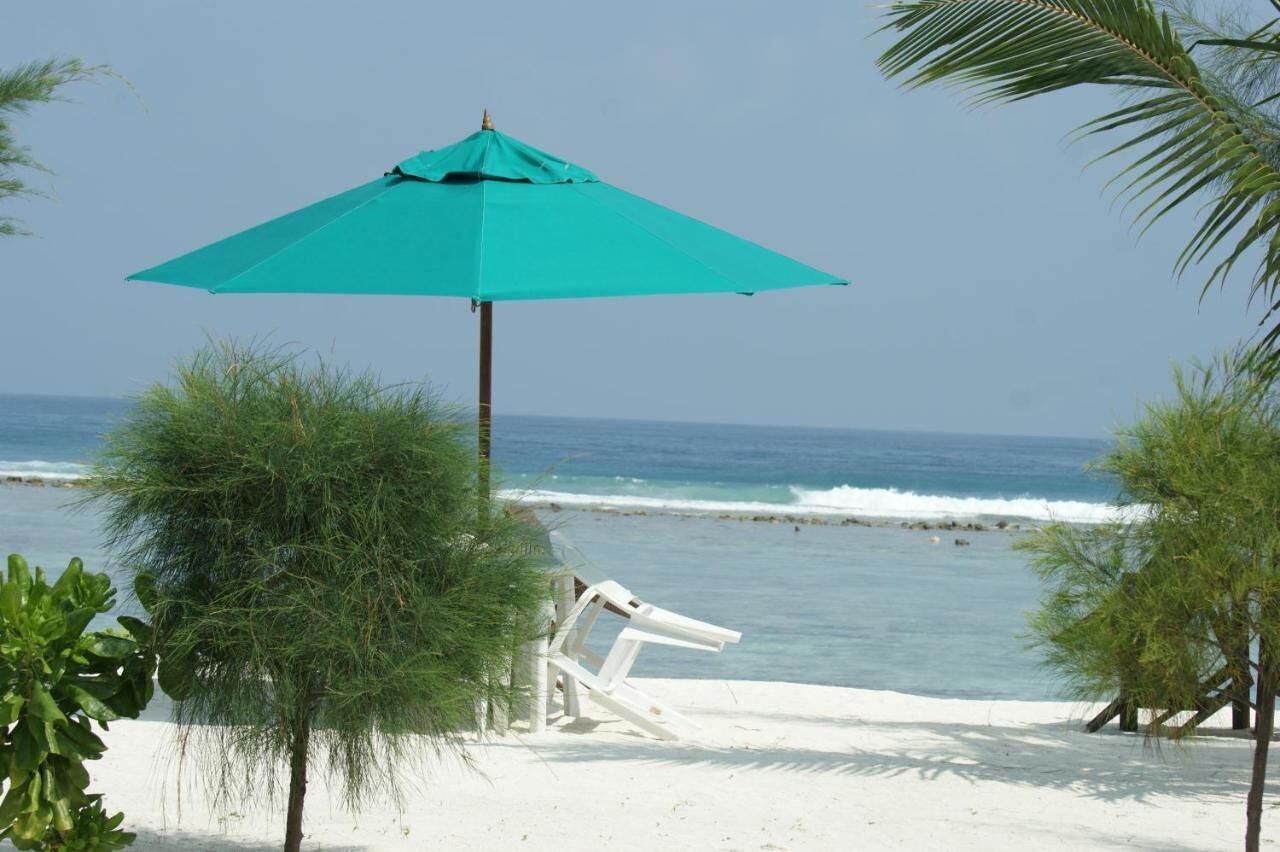 Una playa con un paraguas turquesa, sillas de playa blancas y palmeras.