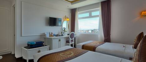 A hotel room with two beds, a desk with a TV, a window with a view, and a cityscape.