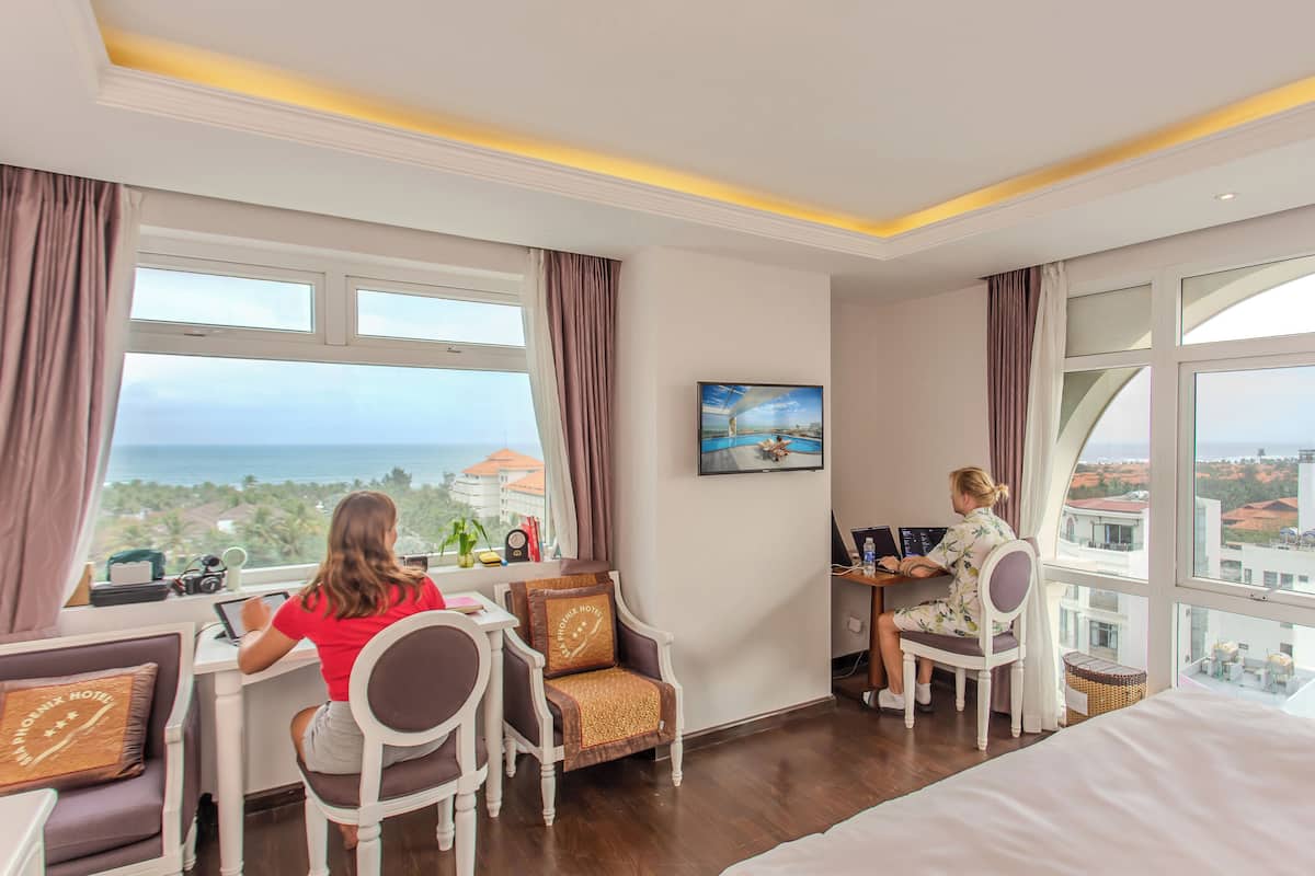 Une chambre d’hôtel avec une grande fenêtre, un bureau, une chaise et un lit.