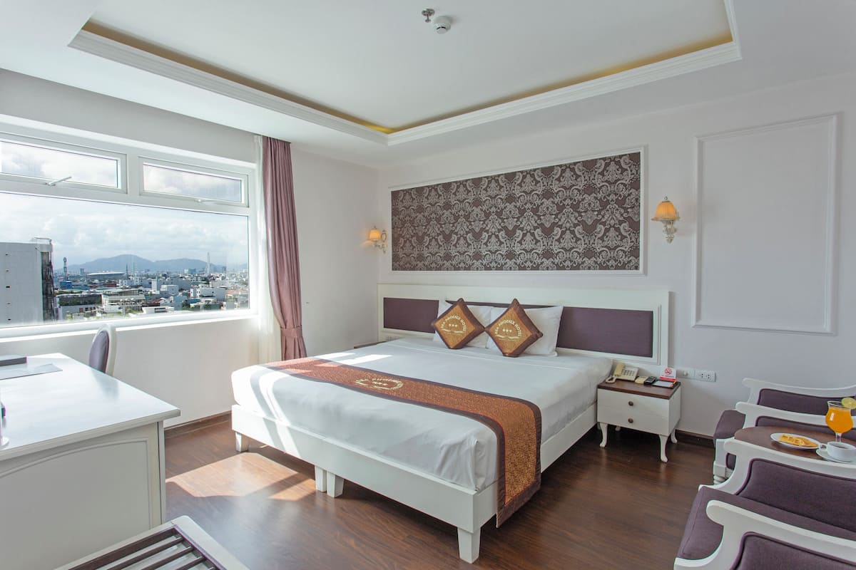 Une chambre d’hôtel avec un grand lit, un bureau et une chaise. Il y a une fenêtre donnant sur un paysage urbain.