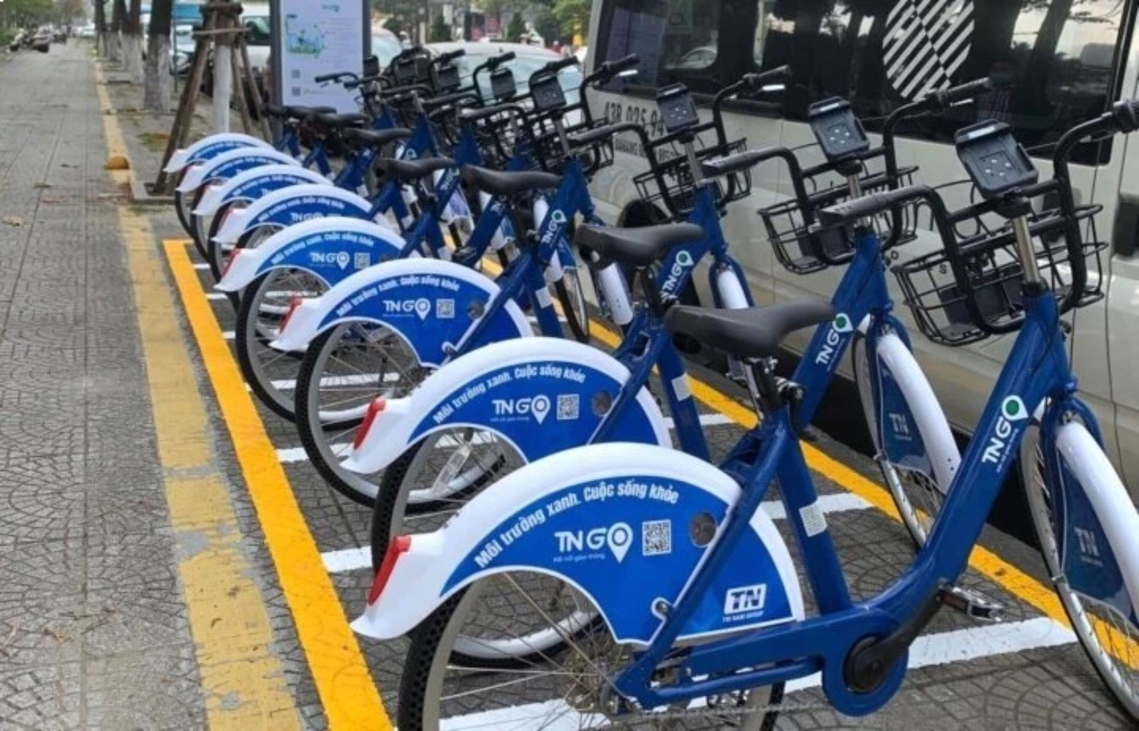 Una fila di biciclette elettriche blu TNG parcheggiate lungo un marciapiede.