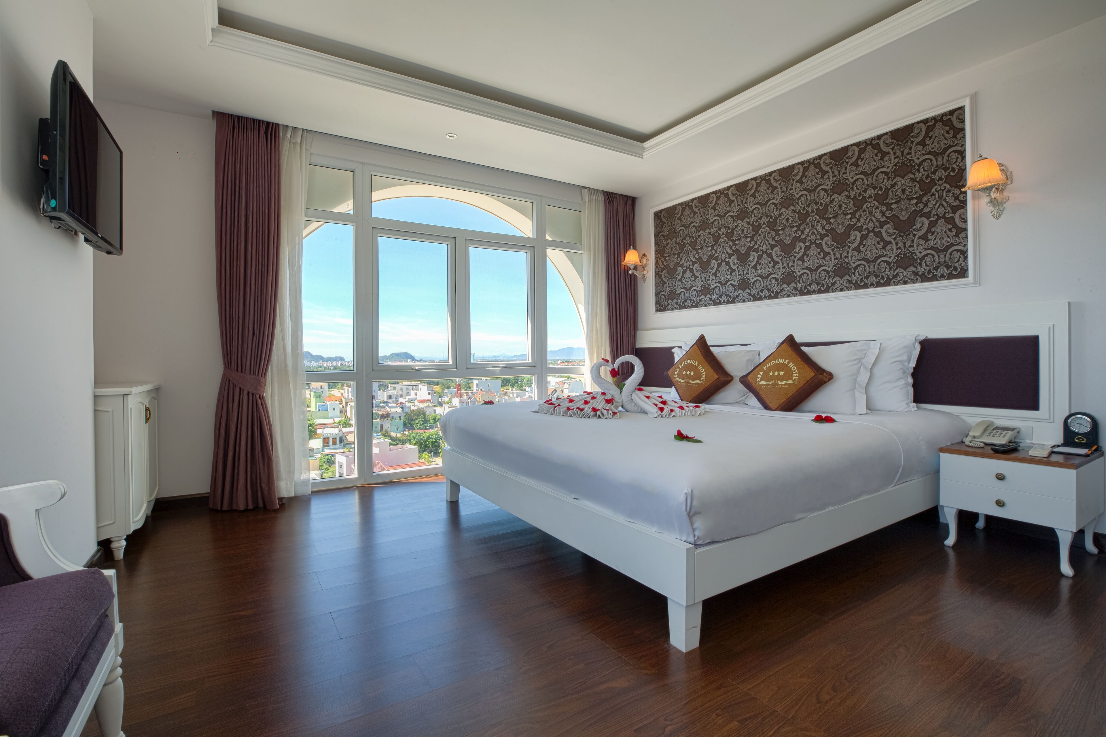 Um quarto espaçoso com uma cama grande, mesa de cabeceira, televisão e vista para a cidade.