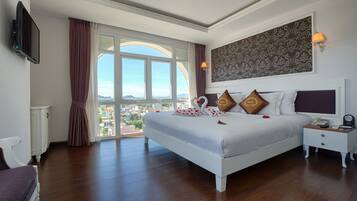 Um quarto espaçoso com uma cama grande, mesa de cabeceira, televisão e vista para a cidade.