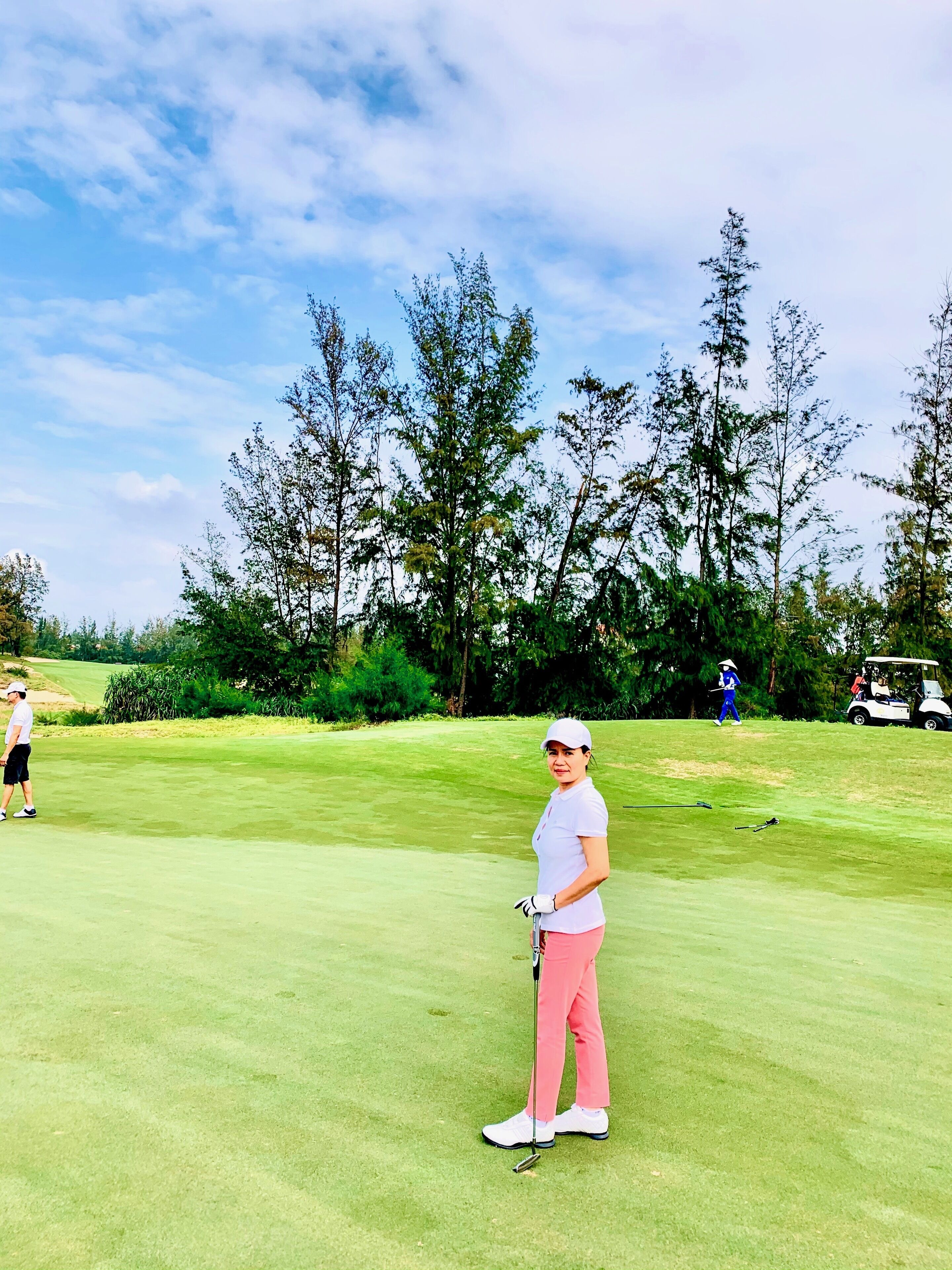 A golf course with a well-maintained green, trees, and a clear sky.