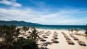 A beach with thatched umbrellas and palm trees, a clear sky, and the ocean in the background. - Sea Phoenix Hotel Da Nang (Da Nang)