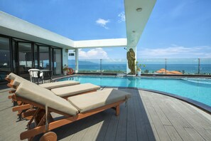 A poolside area with sun loungers, a statue, and a view of the ocean. - Sea Phoenix Hotel - My Khe Beach Da Nang (Da Nang)