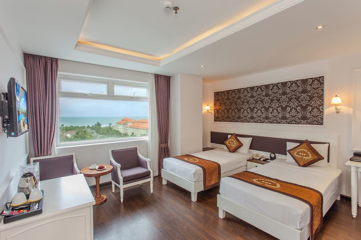 Une chambre d’hôtel avec deux lits, un bureau, des chaises, une vue sur l’océan et un panneau décoratif mural.