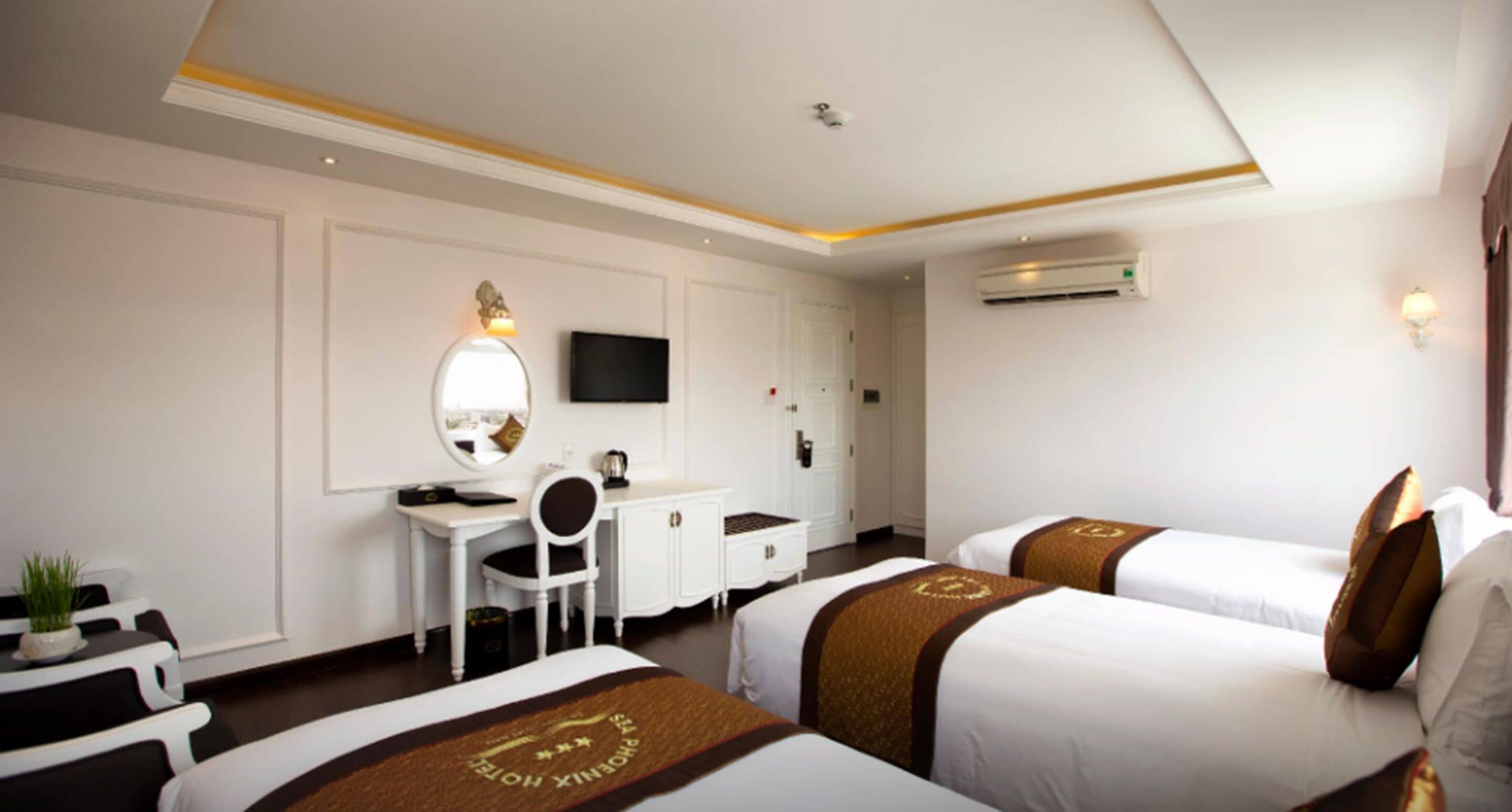 A hotel room with two beds, a desk, a chair, a mirror, a television, and an air conditioning unit.