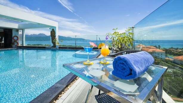 A glass-top pool table with a blue towel, a cocktail, and a drink with a straw, overlooking a scenic ocean view. - Sea Phoenix Hotel Da Nang (Da Nang)