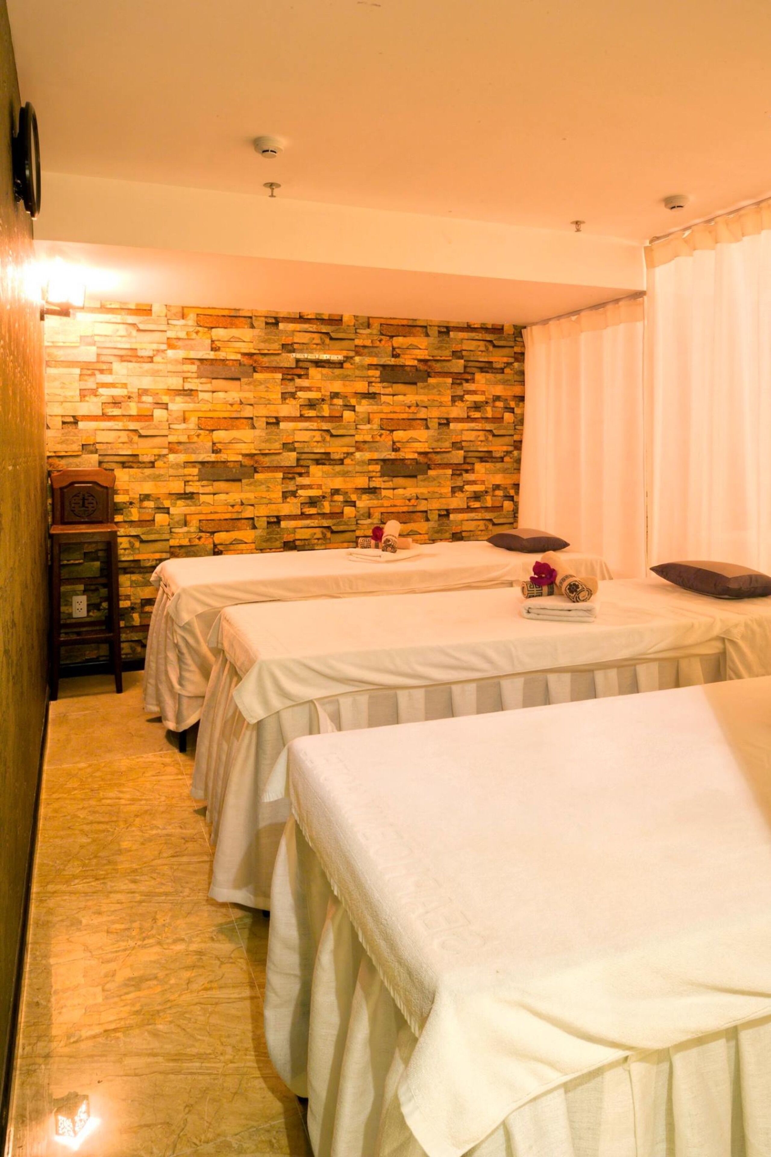 Un cuarto de spa con dos camas, una pared de piedra, un reloj y una pequeña mesa con toallas y una flor.