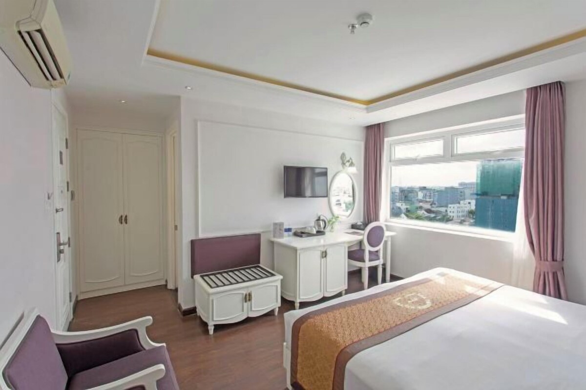 Habitación de hotel con cama, escritorio con silla, tocador con espejo y ventana con vista a la ciudad.