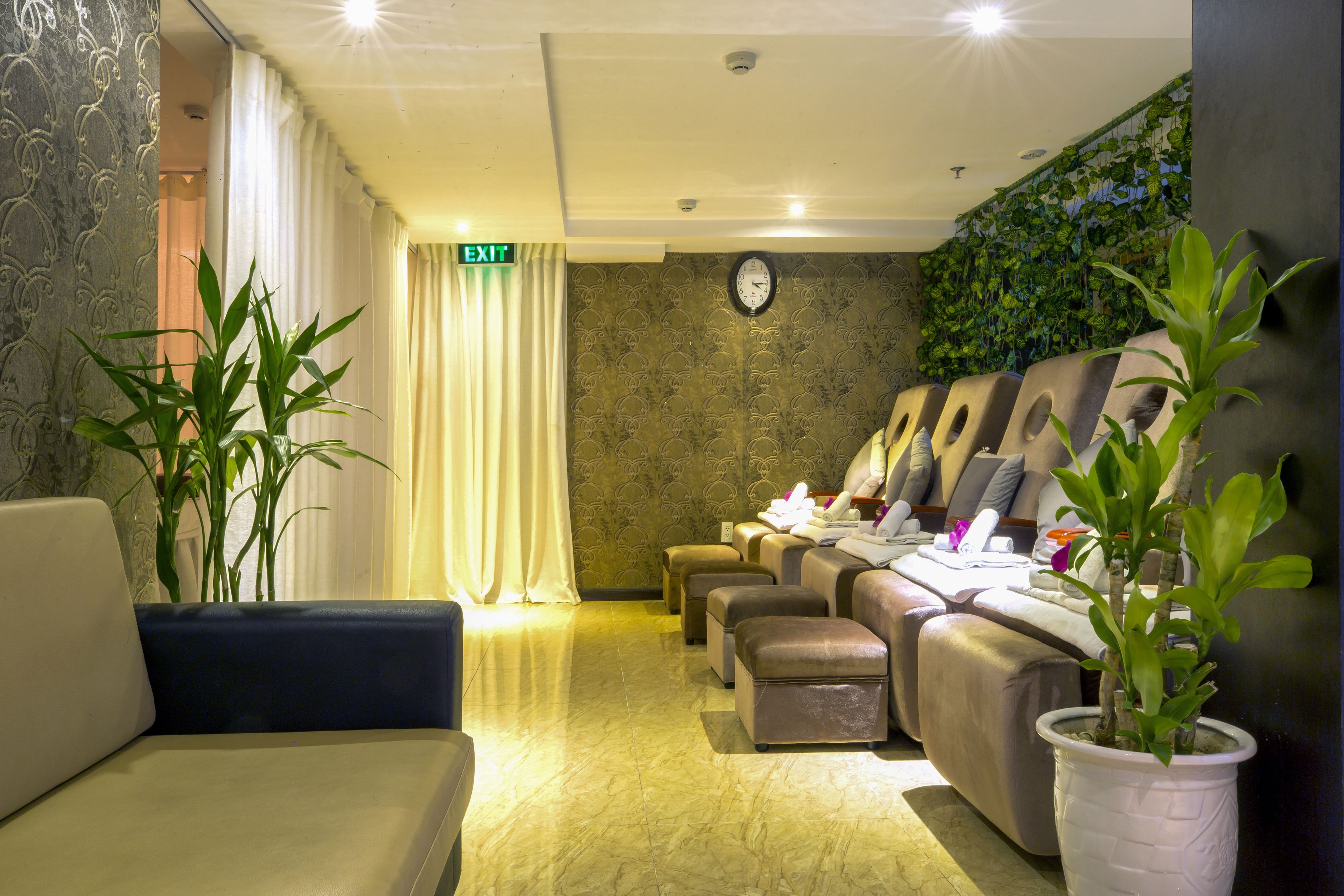 A reception area with a sofa, a massage chair, a clock, and a wall with greenery.