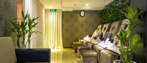 Een receptiezone met een bank, een massagestoel, een klok en een wand met beplanting.