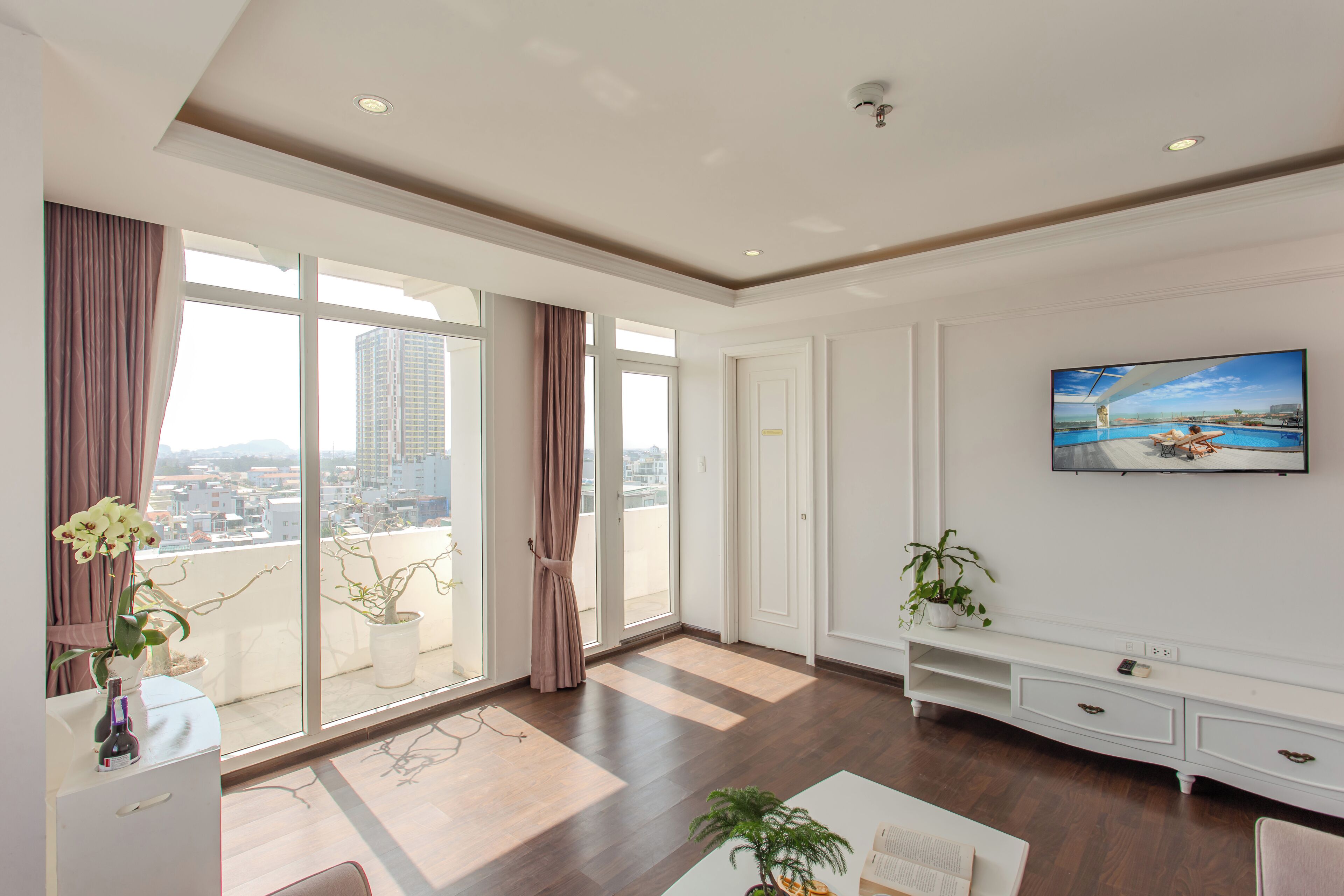 Un salón espacioso con un gran ventanal, un televisor de pantalla plana en la pared y un balcón con plantas en macetas.