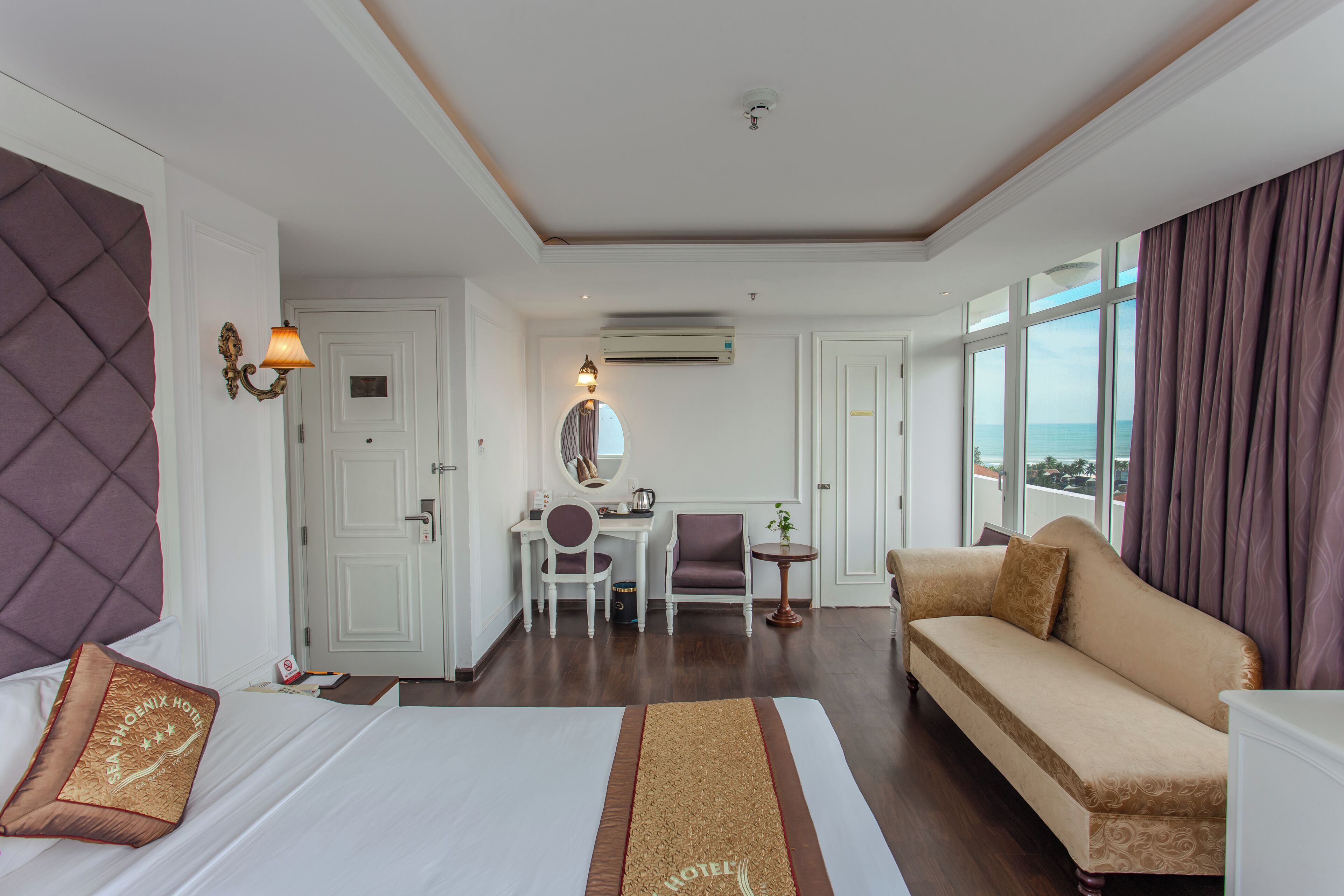 A hotel room with a bed, a sofa, a desk with a chair, a small table, and a large window offering a view.