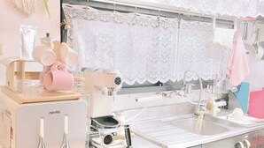 Una cocina con cafetera, lavamanos y un cortinilla de encaje.