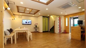 Un salon chaleureux avec un plancher en bois, un coin repas avec une table et des chaises, un téléviseur fixé au mur et un escalier menant à un autre niveau.