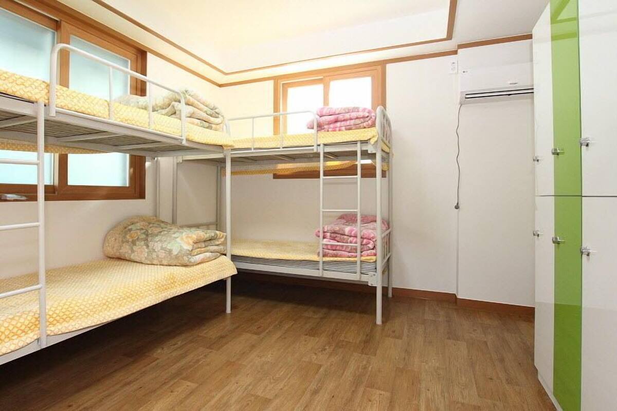 Une chambre avec un lit superposé, une fenêtre, une armoire et un plancher en bois.