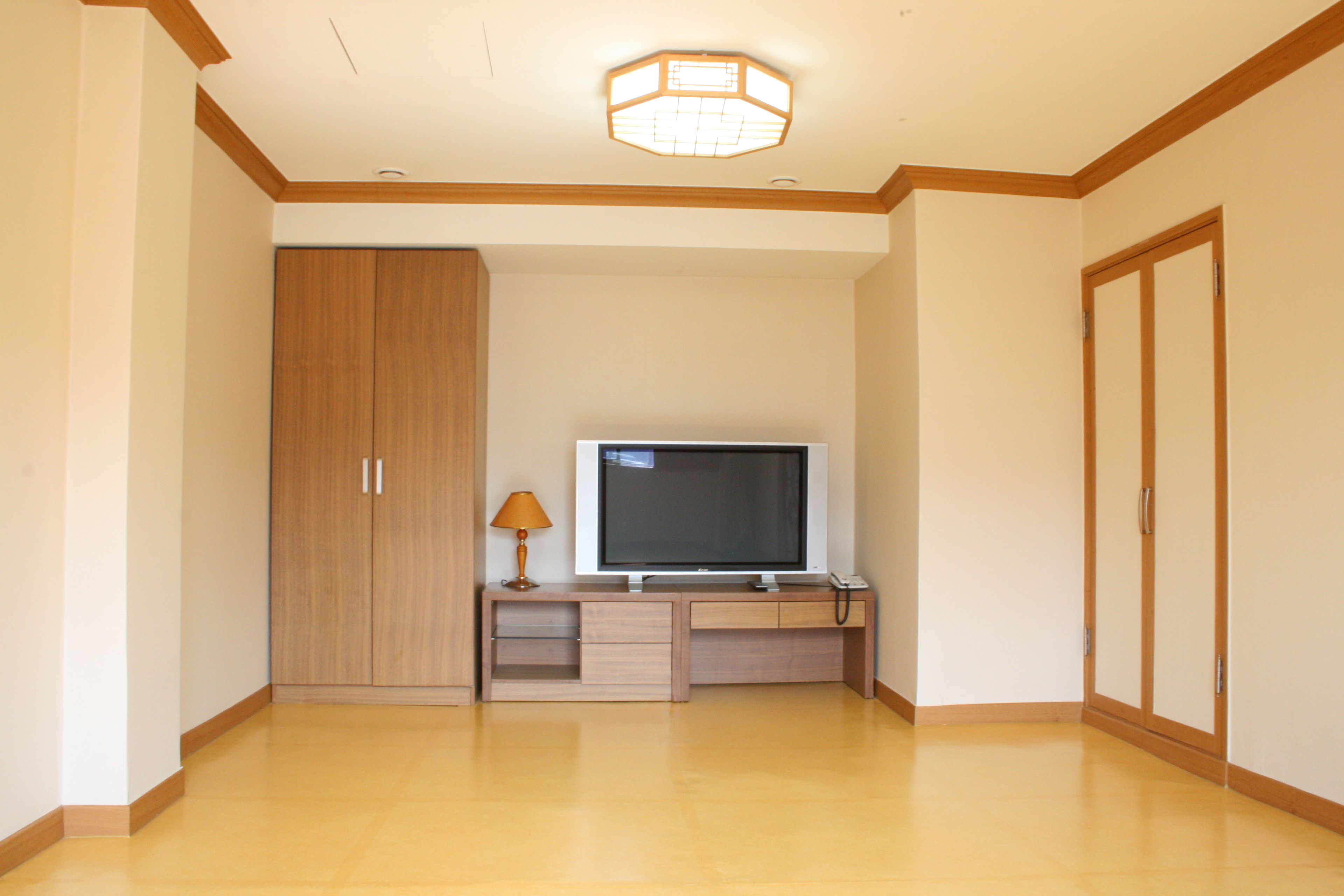 Una habitación con un armario de madera, un televisor sobre un mueble de madera y una lámpara.