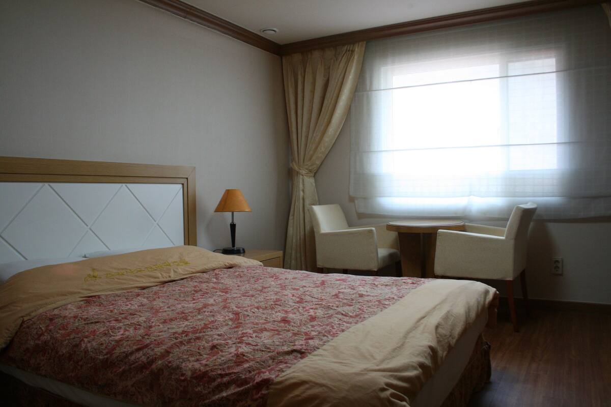 A hotel room with a bed, a desk, a chair, and a window with curtains.