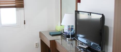 Una habitación de hotel con un escritorio de madera, un televisor, una lámpara y un espejo.