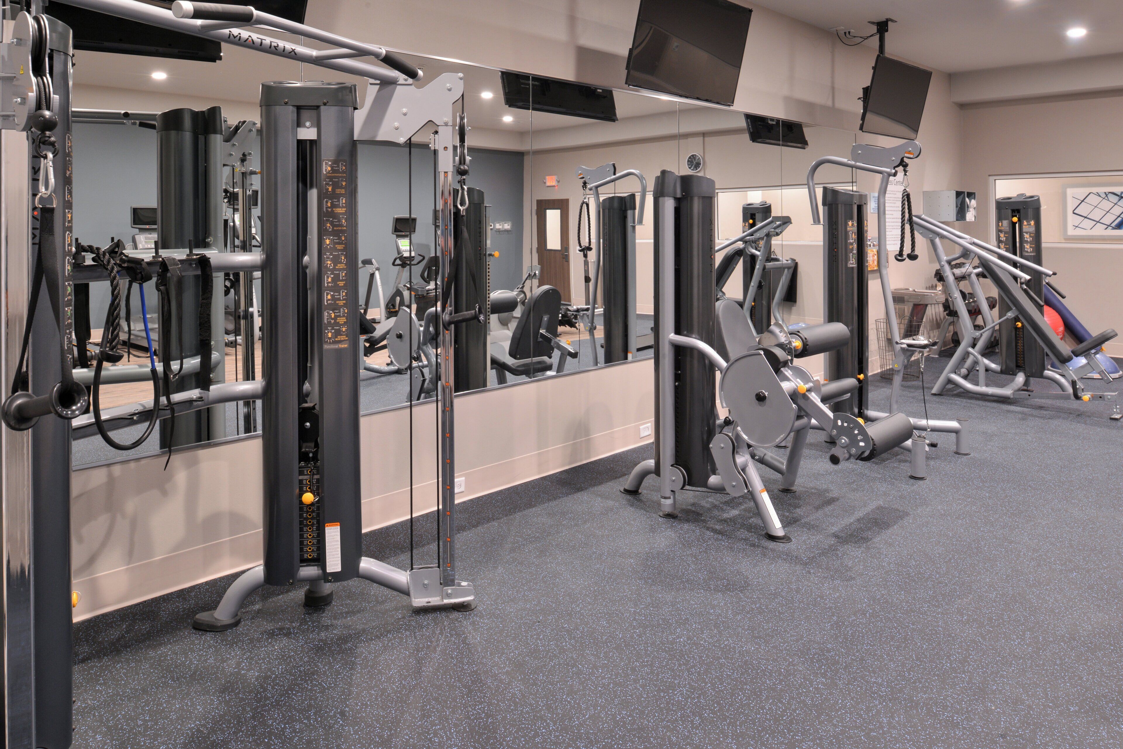 A gym with various exercise machines, mirrors, and a carpeted floor.