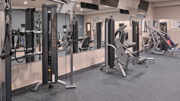 A gym with various exercise machines, mirrors, and a carpeted floor.