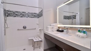 A modern bathroom with a walk-in shower, a glass shower enclosure, a vanity with a large mirror, and neatly stacked towels.