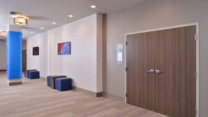 A hallway with a wooden door, blue seating, and wall-mounted artwork.