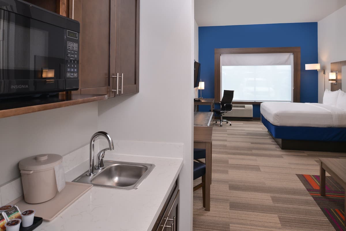 A modern hotel room with a kitchenette, a bed, a desk, and a large window.