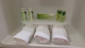 A bathroom shelf with three white towels and three bottles of lotion.
