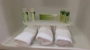 A bathroom shelf with three white towels and three bottles of lotion. - Holiday Inn Express & Suites Houston E - Pasadena by IHG (Pasadena)