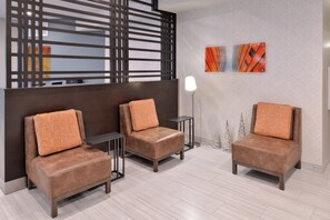 Un espace salon moderne avec trois fauteuils marron et une petite table d’appoint, un panneau décoratif mural et deux œuvres d’art encadrées.