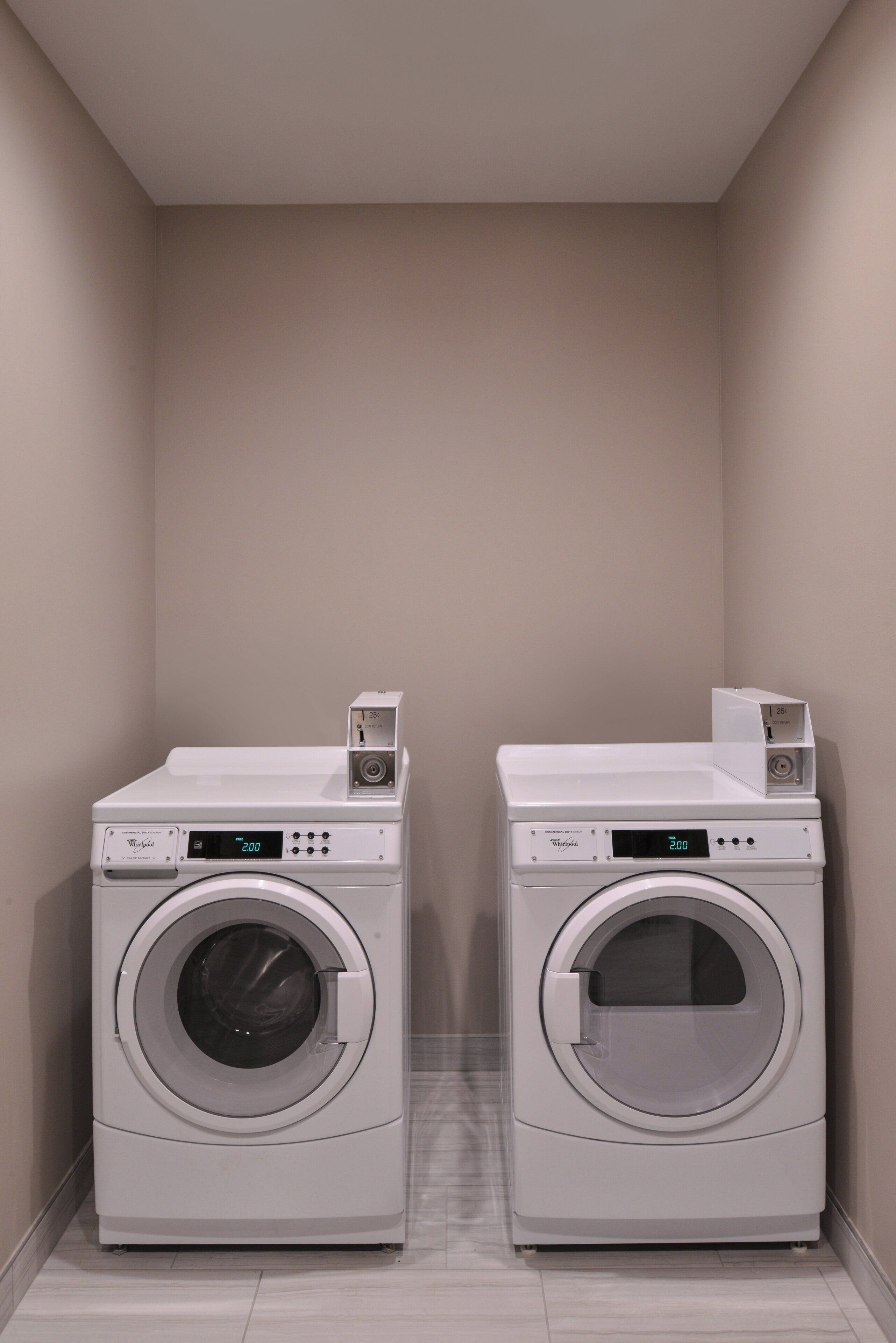 Two front-loading Whirlpool washers in a laundry room with a tiled floor and plain walls.