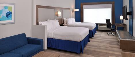 Habitación de hotel con dos camas, un sofá azul, una mesita, un escritorio con una silla y un televisor.