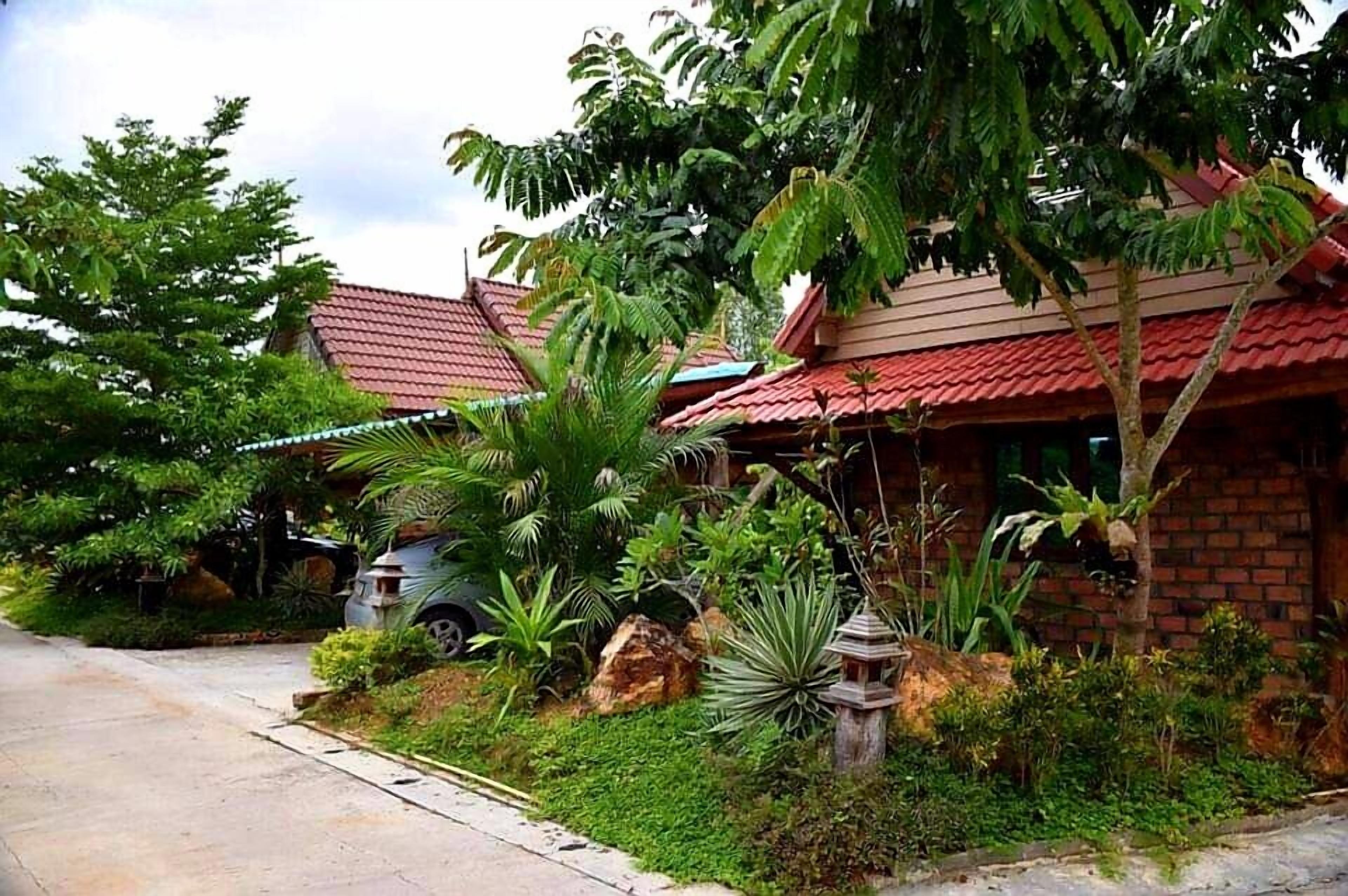 A residential area with houses featuring red roofs and lush greenery, including palm trees and various plants.