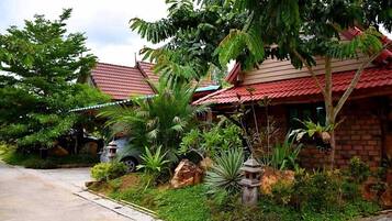 A residential area with houses featuring red roofs and lush greenery, including palm trees and various plants.