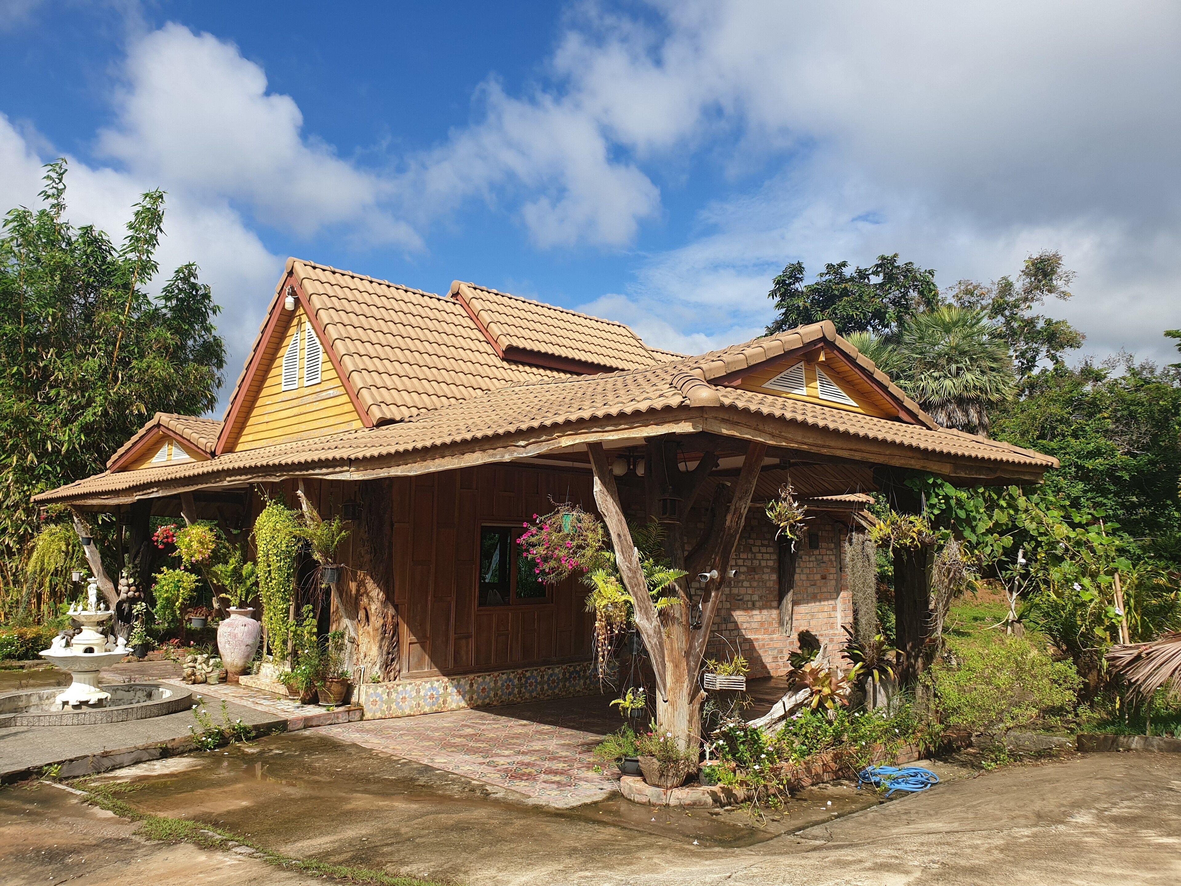 A two-story house with a tiled roof, wooden beams, and a garden with a fountain.