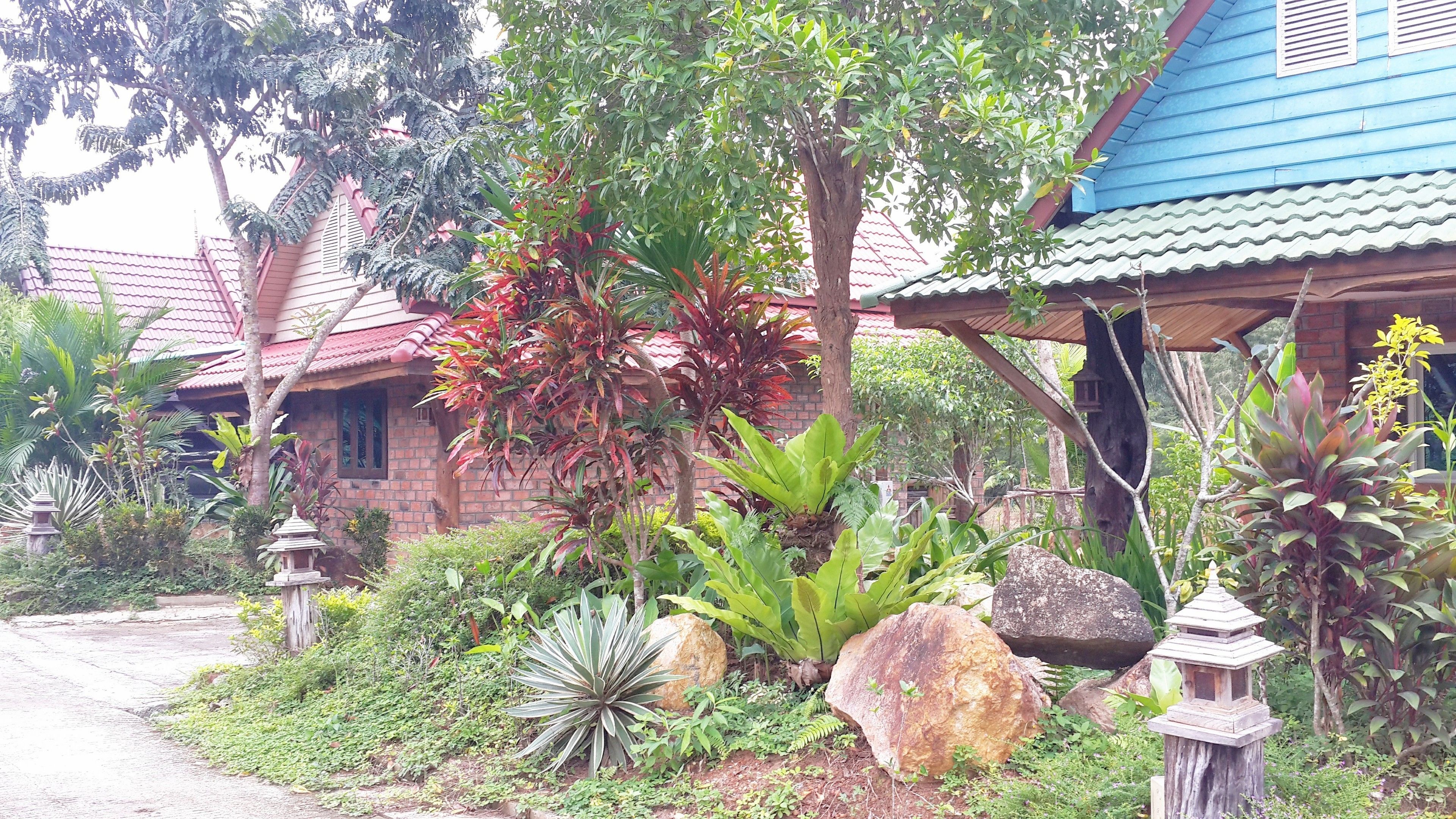Una casa tradicional con tejado de tejas rojas, rodeada de abundante vegetación y grandes rocas.
