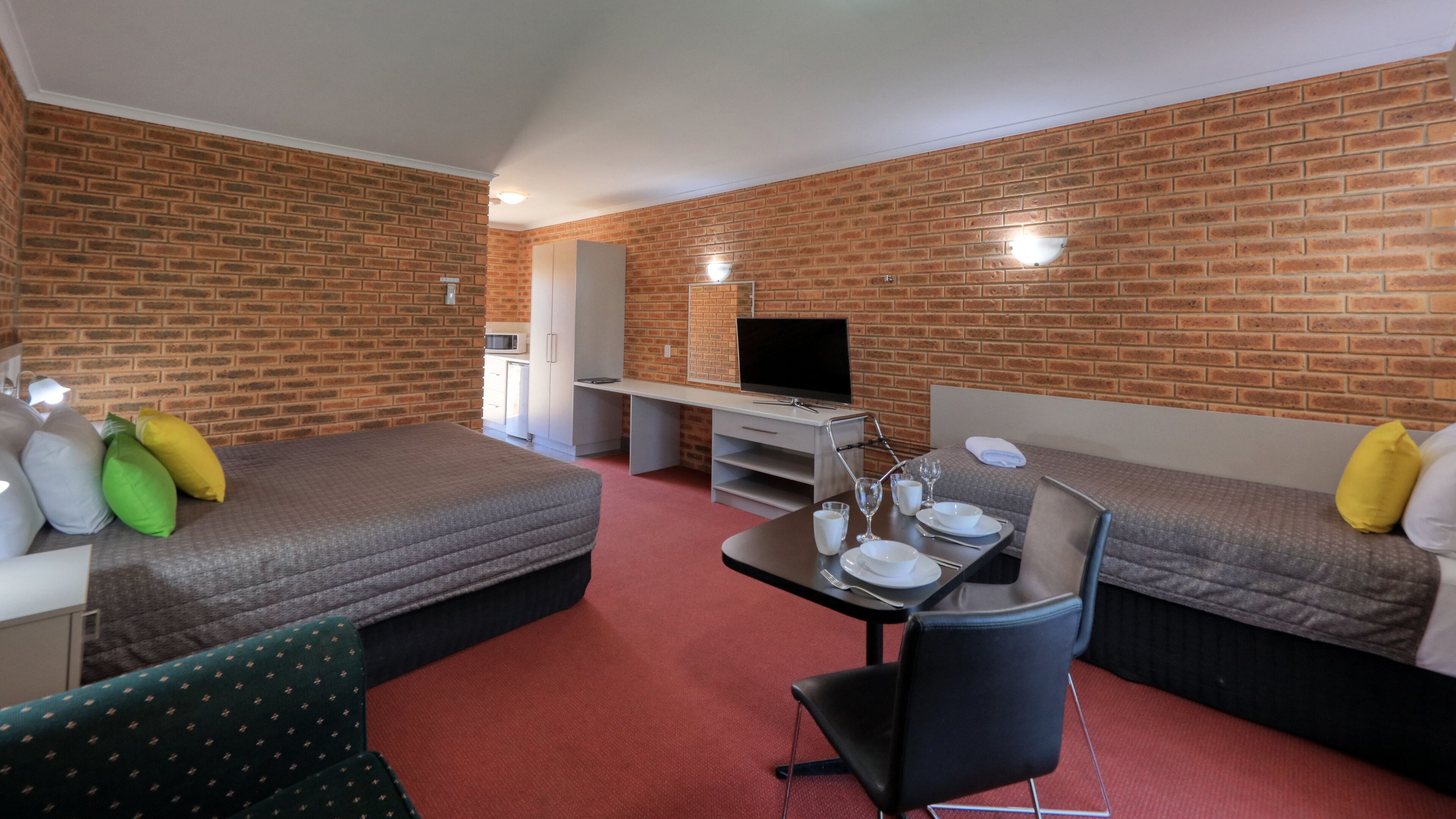 A hotel room with two beds, a dining table, a TV, and a kitchenette.