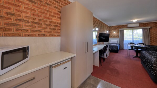 A compact hotel room with a kitchenette, a bed, a TV, and a dining area.