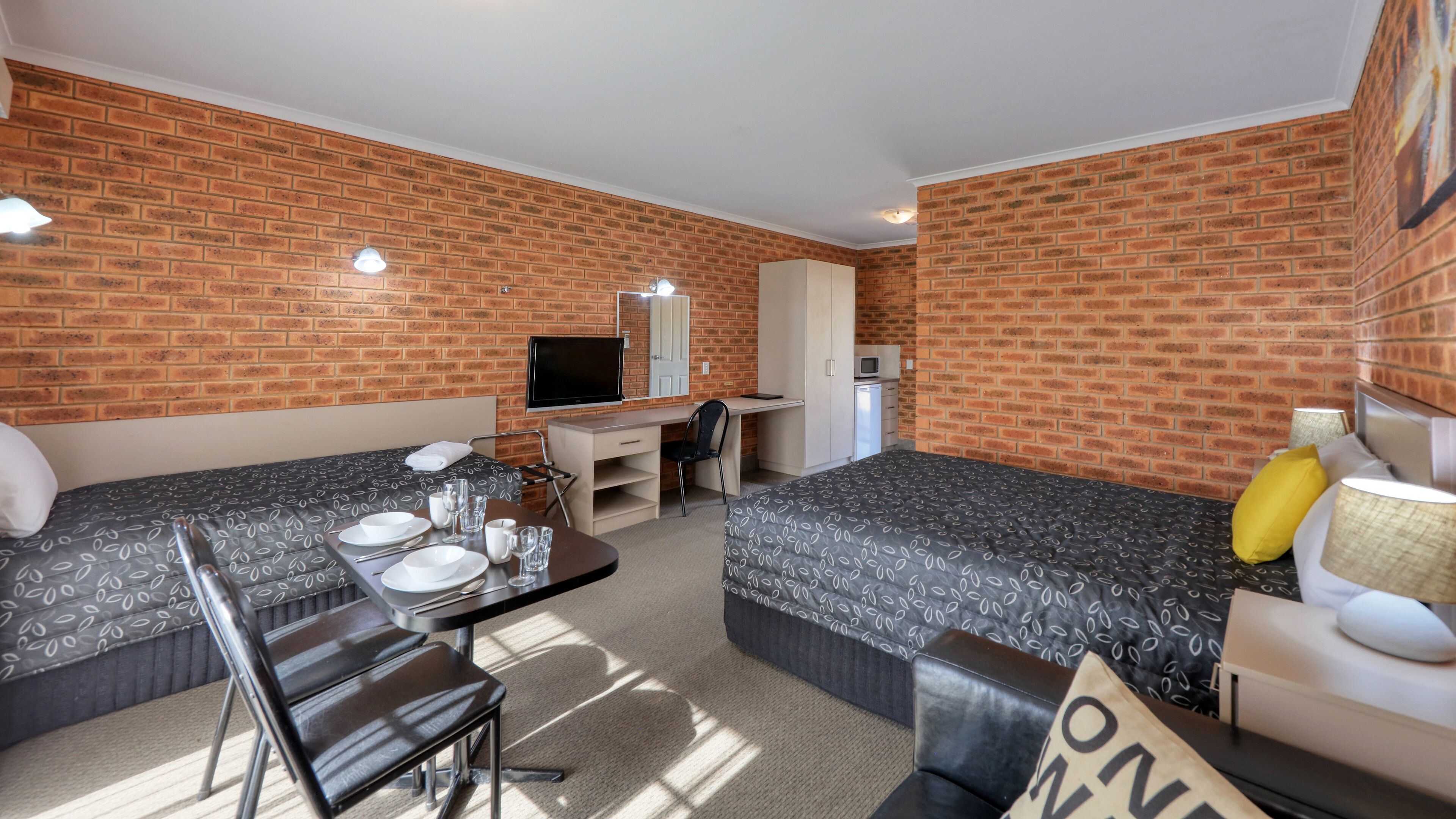 Una habitación de hotel compacta con dos camas individuales, un escritorio, una silla, un televisor y una pequeña kitchenette.