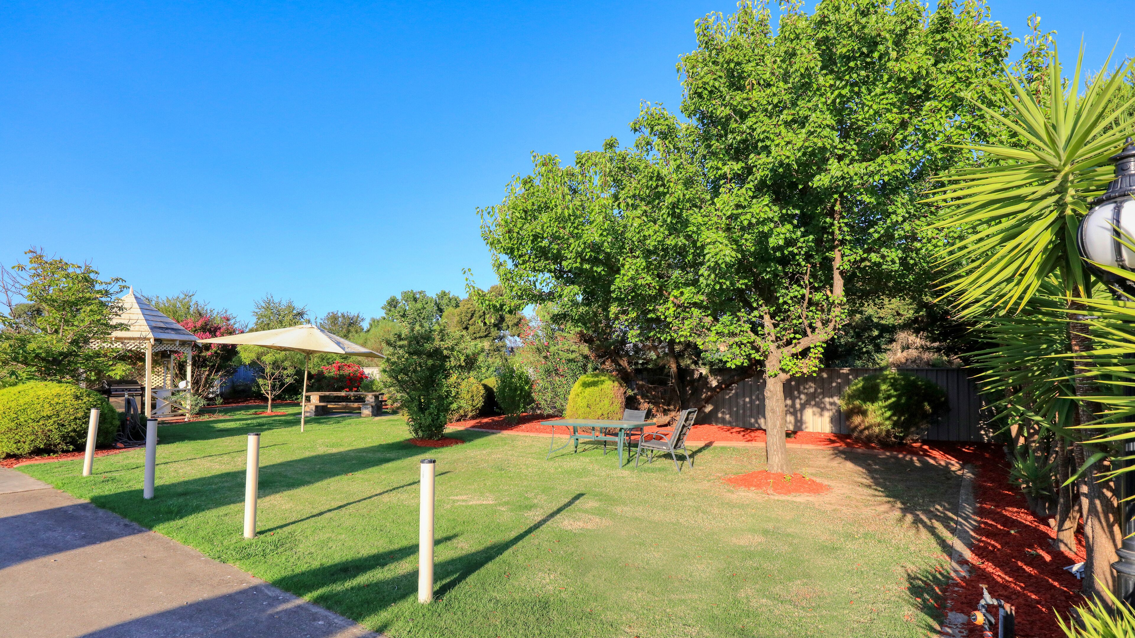 Un giardino curato con un gazebo, un tavolo da picnic e diverse piante e arbusti.