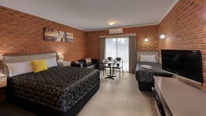Une chambre d’hôtel avec un mur en briques, un lit avec une literie à motifs, un bureau avec une télévision et un coin repas avec des chaises et une table.