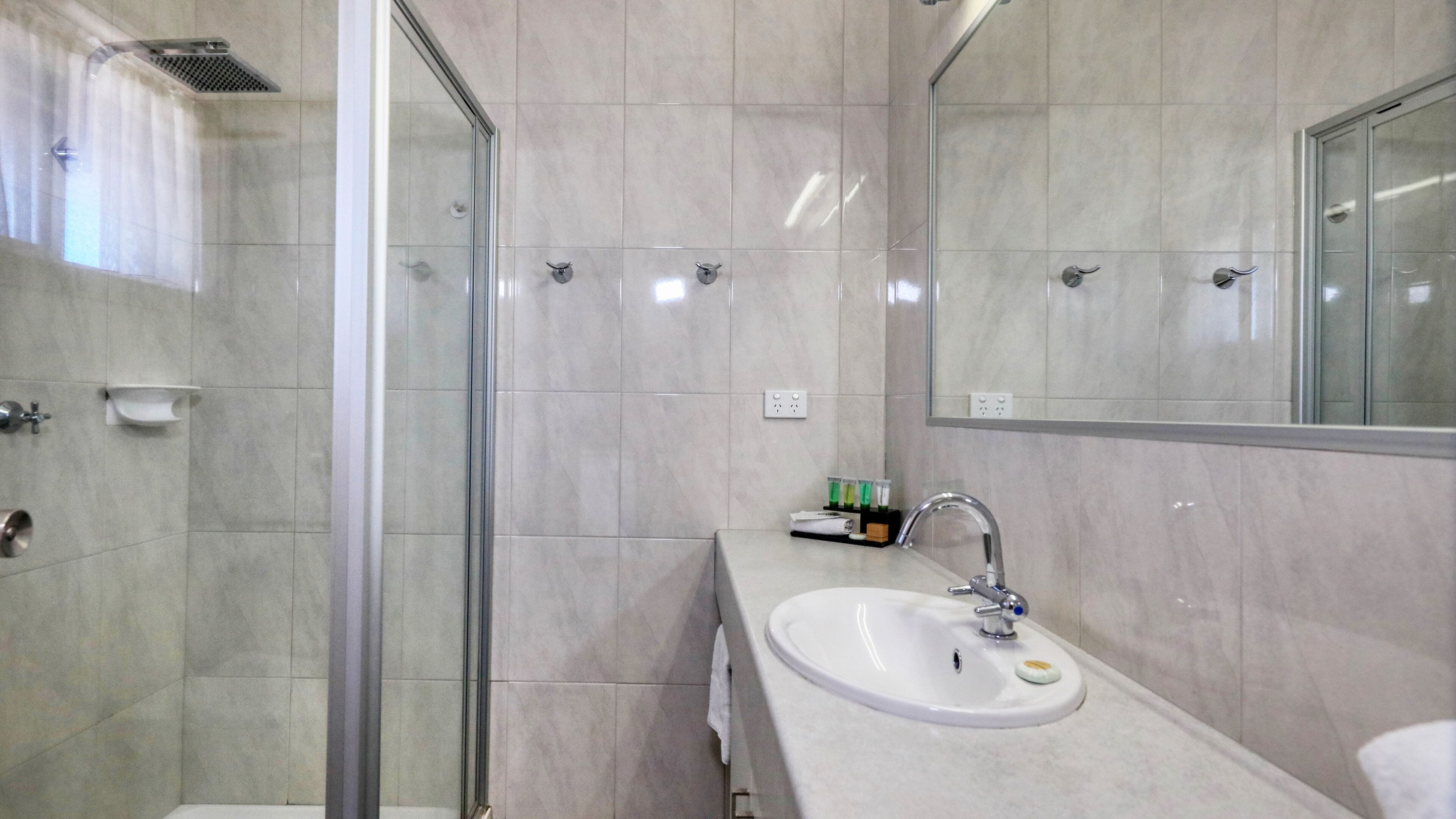 Un bagno moderno con cabina doccia in vetro, lavandino bianco con specchio e parete rivestita di piastrelle.