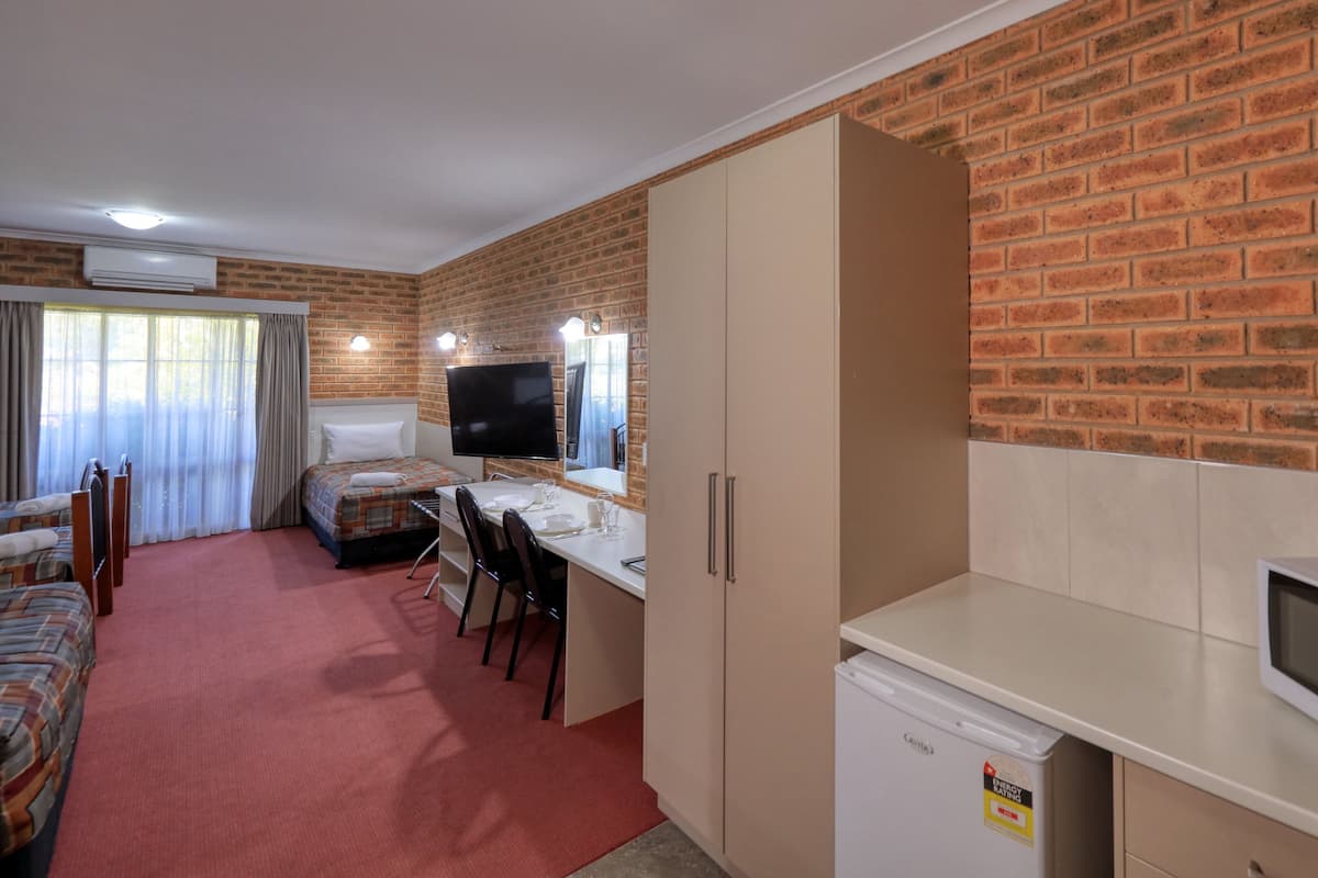 Une pièce de taille modeste avec un mur en briques, un lit, un bureau avec une télévision, un four à micro-ondes et un petit réfrigérateur.