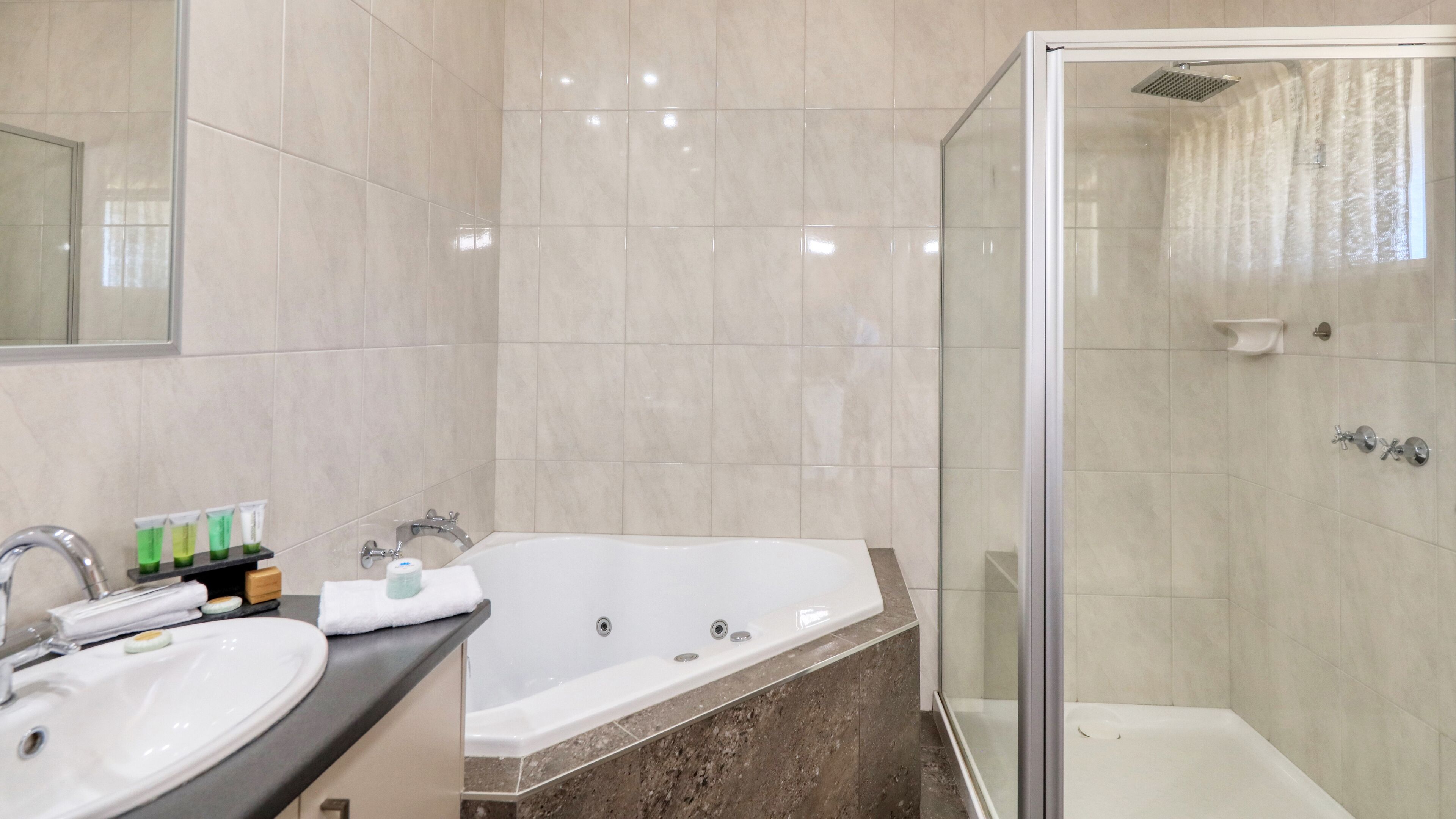 A modern bathroom with a large bathtub, a separate shower area, and a vanity with a sink and toiletries.